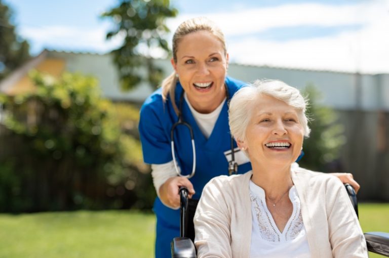 Elder woman sitting on wheelchair with caregiver pushing her