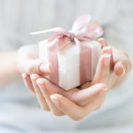Close up shot of female hands holding a small gift wrapped with pink ribbon