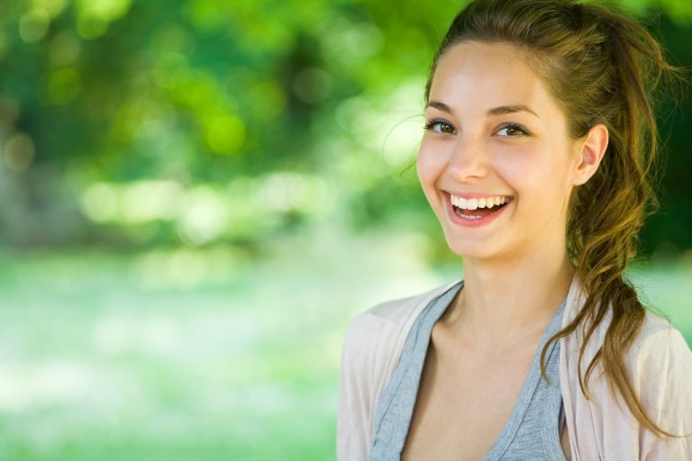 young teenager smiling outdoors with blurred trees in background