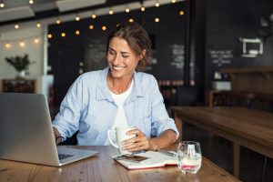 Smiling woman working on a laptop while sitting inside a coffee shop.
