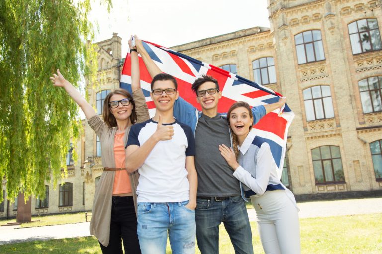 Group of students smiling in front of a school building while carrying a British flag.